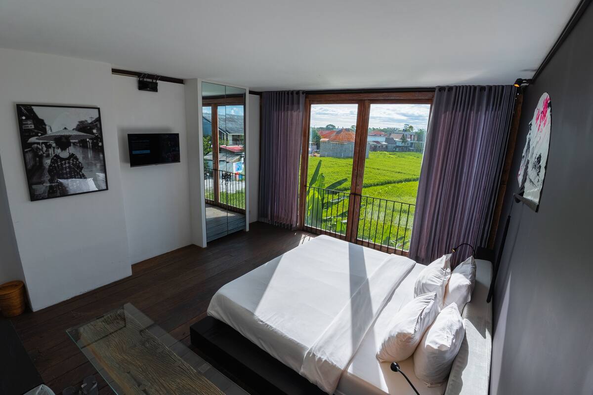 Un dormitorio moderno con una cama grande, una mesa de centro de vidrio y vistas a un campo verde por la ventana.