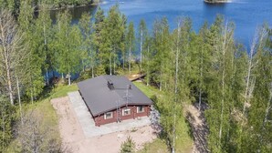 Une cabane avec un toit en métal, entourée d’une forêt dense et d’un grand lac.