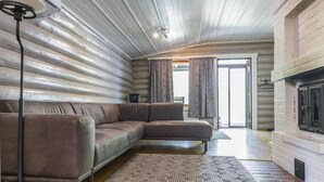 L’intérieur d’une cabane en rondins, avec un canapé d’angle, un tapis à motifs, une cheminée et une grande fenêtre agrémentée de rideaux.