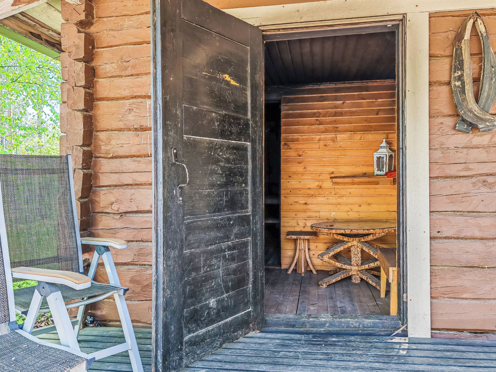 A wooden cabin entrance with a large door, a chair, and a small table inside.
