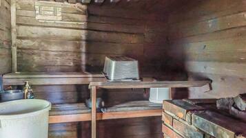 Interior rústico de una cabaña de madera con un horno de metal, un estante con una caja y un contenedor metálico grande.