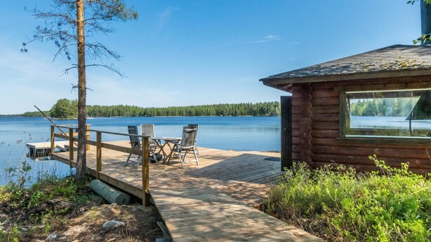 Une jetée en bois mène à un chalet doté d’une grande fenêtre donnant sur un lac.
