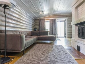 Ein Blockhaushaus-Interieur mit einer Eckcouch, einem gemusterten Teppich, einem Kamin und einem Deckenventilator.