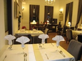 A hotel dining area with tables set for service, a television in the background, and a seating area with chairs and tables.