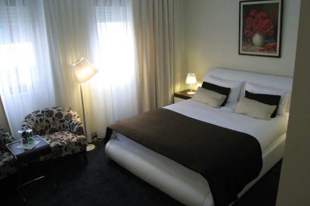Una habitación de hotel con una cama, una silla, un escritorio y una lámpara.