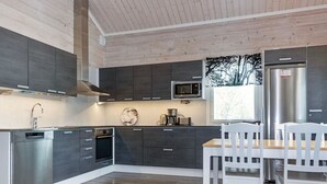 A modern kitchen with dark cabinets, stainless steel appliances, and a wooden dining table with white chairs. - Mökki tenolla by Interhome (Utsjoki)