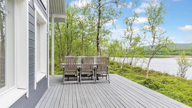 A wooden deck with a table and chairs, overlooking a lake and surrounded by trees. - Mökki tenolla by Interhome (Utsjoki)