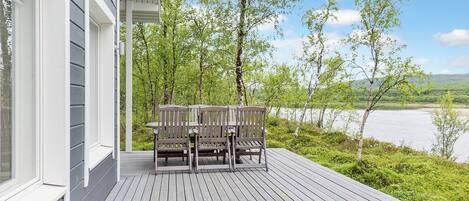 A wooden deck with a table and chairs, overlooking a body of water and trees.
