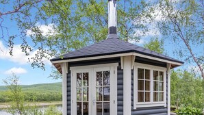 A small log cabin with a chimney, large windows, and a view of a lake and hills. - Mökki tenolla by Interhome (Utsjoki)