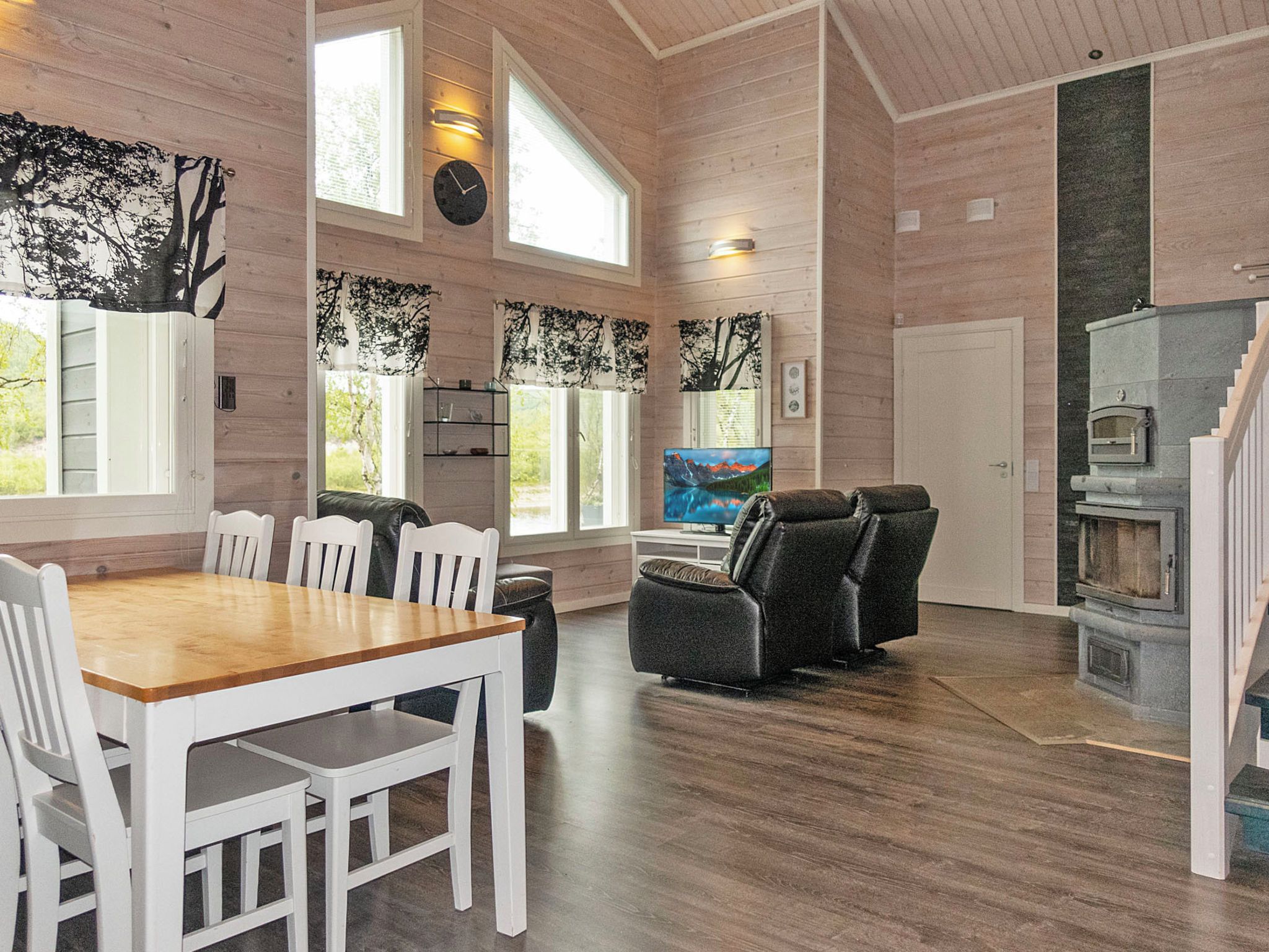 A spacious room with a wooden floor, a dining table with chairs, a sofa, a fireplace, and large windows.