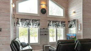 A cozy room with two leather sofas, a small table, and a TV. Large windows with curtains are visible, and a clock is mounted on the wall. - Mökki tenolla by Interhome (Utsjoki)
