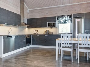 A modern kitchen with dark cabinets, stainless appliances, and a dining area with white chairs. - Mökki tenolla by Interhome (Utsjoki)