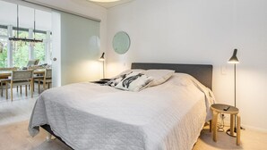A modern bedroom with a large bed, bedside lamps, and a view of the outdoors through a large window.