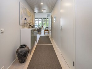 Een gang met een vloerkleed, een kast, een vaas en een schilderij aan de muur.