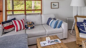 A cozy living room with a large window, a sofa with striped cushions, a wicker chair, and a small table with a tray.