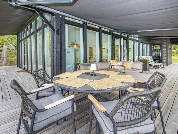 Un patio exterior con una mesa redonda y sillas, rodeado por amplios ventanales.