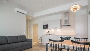 Un apartamento moderno con un sofá gris, un comedor con sillas negras y una cocina con armarios blancos.