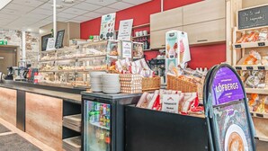 Mostrador de una panadería con diversos productos horneados, una máquina de café y una exhibición de tazas de café.