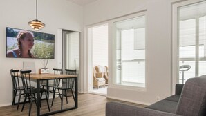 Una sala moderna con una mesa de comedor de madera, sillas negras, un sofá gris y ventanas grandes con persianas.