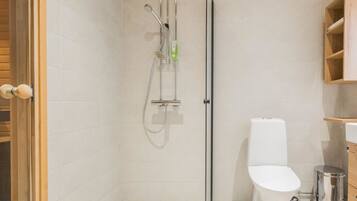 Een moderne badkamer met een douchecabine van glas, een toilet en een kleine prullenbak.