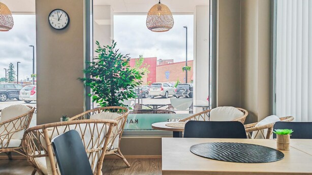 Interior de restaurante con sillas de mimbre, una mesa de madera y vista a la calle a través de amplias ventanas.