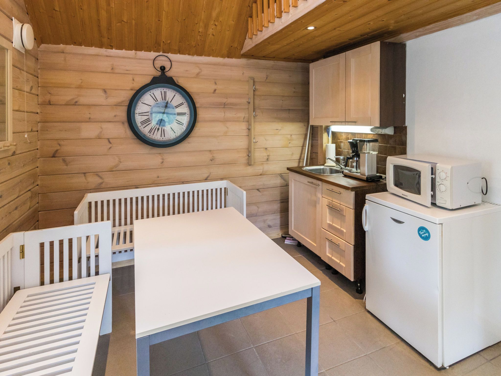 A compact kitchen with wooden walls, a white table, and a clock.