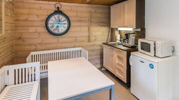 A compact kitchen with wooden walls, a white table, and a clock.