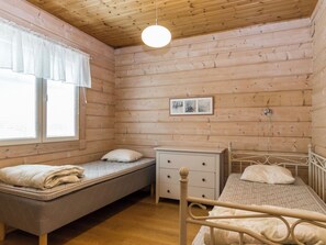 Ein Zimmer mit zwei Betten, einem Nachttisch, einem Fenster mit Vorhängen und einer Pendelleuchte.