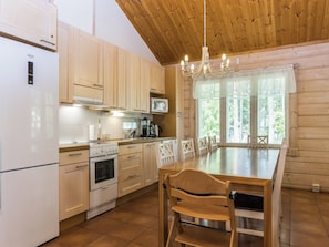 A modern kitchen with wooden cabinets, a built-in microwave, a stove, and a dining area with a table and chairs. - Kuusikko by Interhome (Pori)