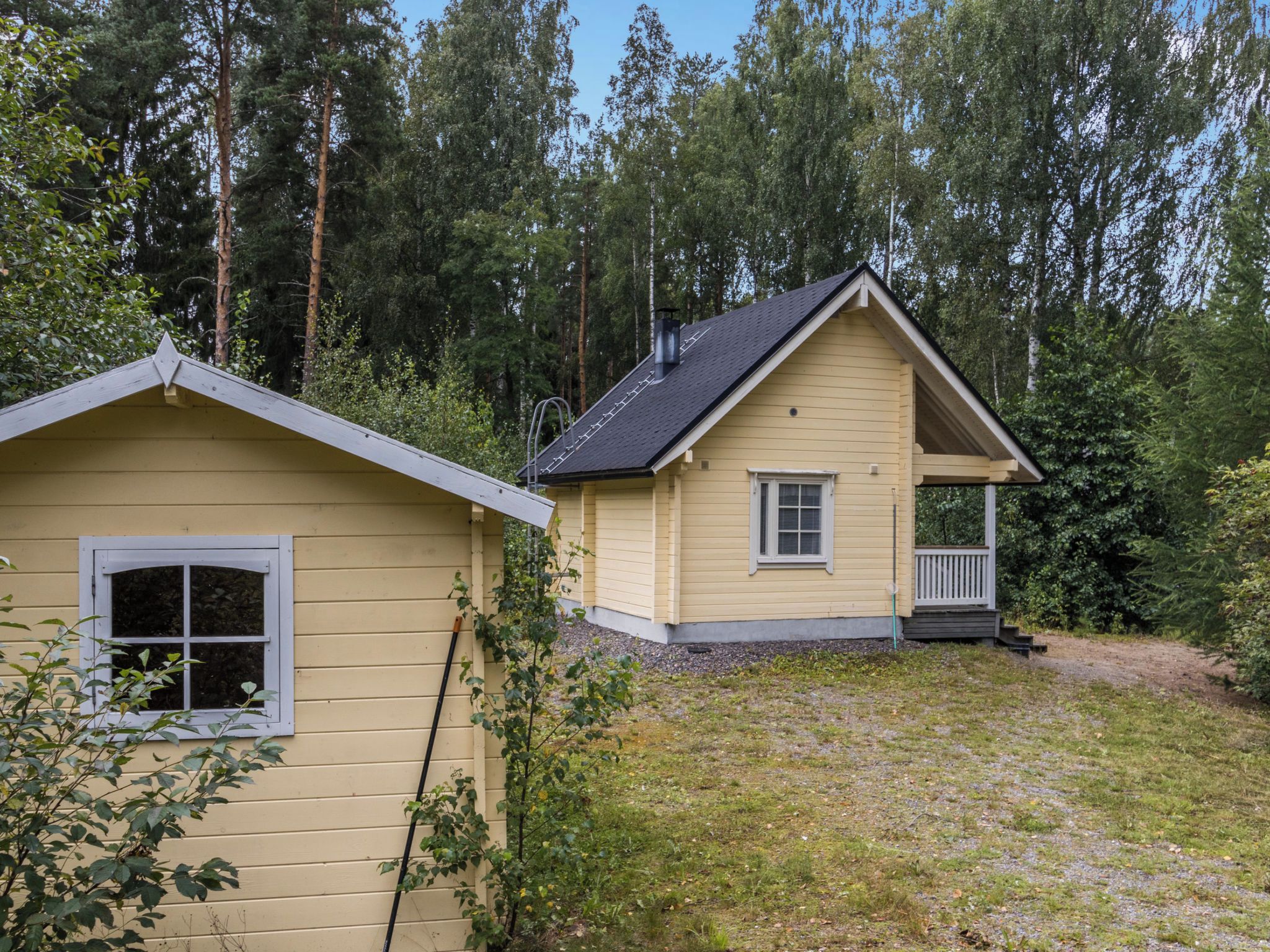 Une maison à deux étages avec un porche, entourée d’une forêt.