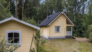 Une maison à deux étages avec un porche, entourée d’une forêt.