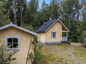 Une maison à deux étages avec un porche, entourée d’une forêt.