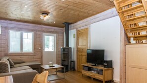 Interior acogedor de una cabaña con techo de madera, un sofá, un televisor, una chimenea y una escalera de madera.