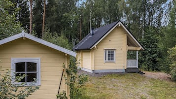 Une maison à deux étages avec un porche, entourée d’une forêt.