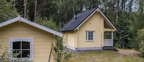 Una casa de dos pisos con un porche, rodeada de bosque.
