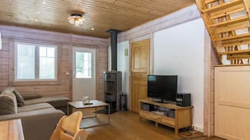 Un intérieur de chalet chaleureux avec un canapé, un téléviseur, une cheminée et un escalier en bois.