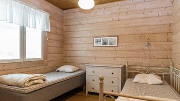 A room with two beds, a nightstand, a window with curtains, and a hanging light fixture.