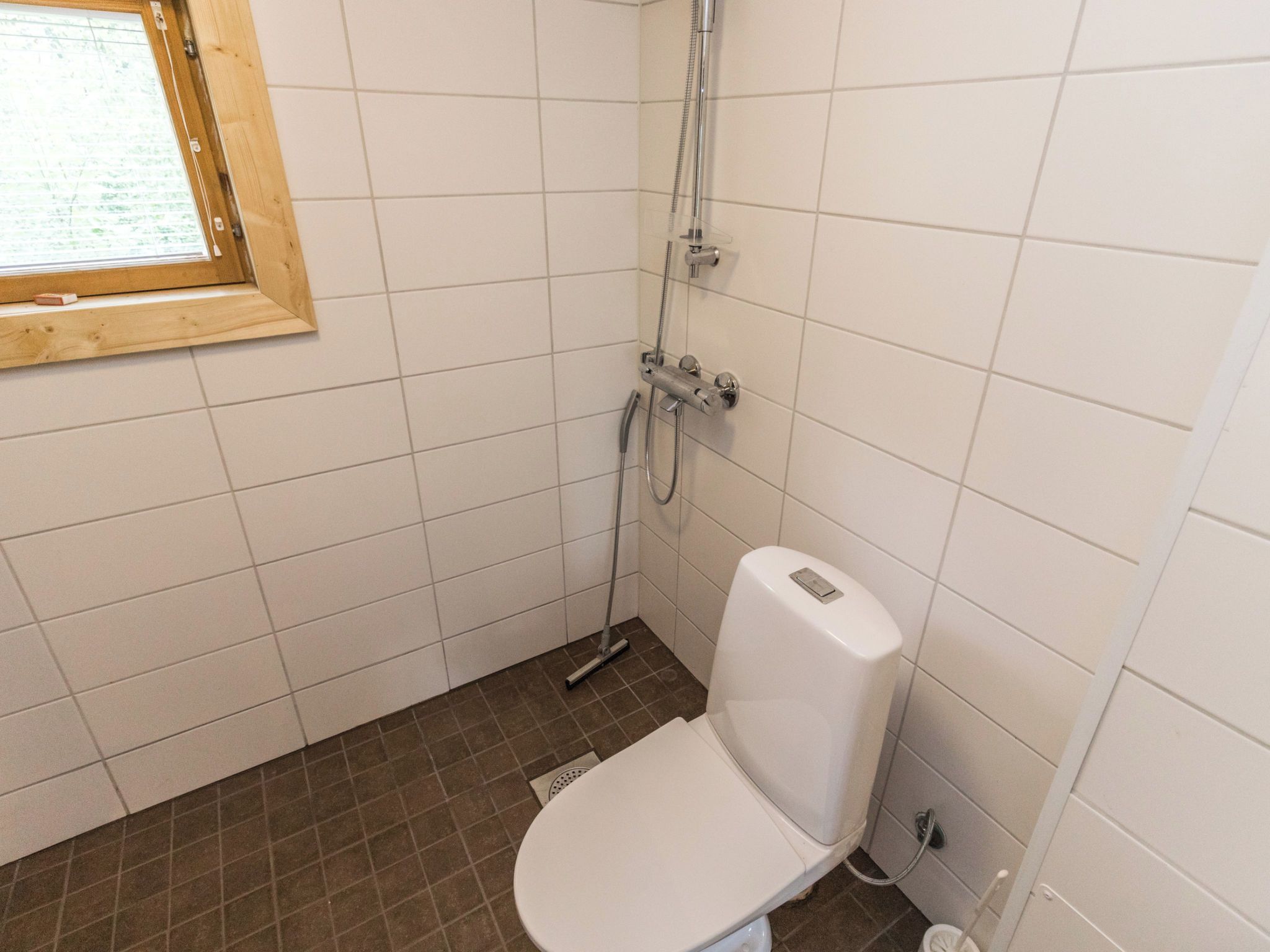 Pieni, laatoitettu kylpyhuone, jossa on wc, suihku ja ikkuna.