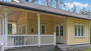 Une maison en bois jaune, dotée d’un porche, de balustrades blanches et d’un petit jardin à l’avant.