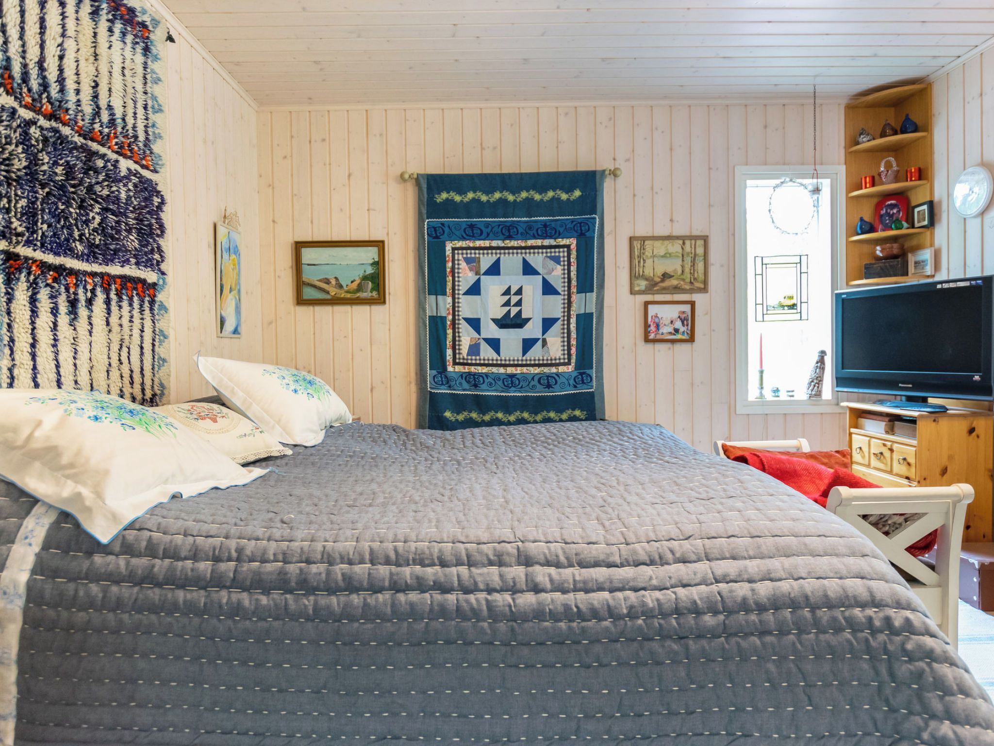 A bedroom with a large bed, a television, and a wooden shelf with decorative items.
