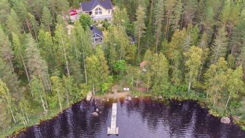 A lakeside cabin surrounded by dense forest, with a dock extending into the water.