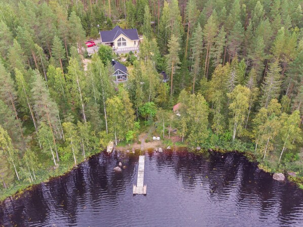 A lakeside cabin surrounded by dense forest, with a dock extending into the water.