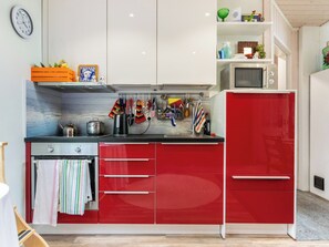 A kitchen with red cabinets, a microwave, and various kitchen utensils.
