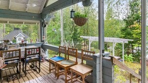 Un espacio al aire libre cubierto con mobiliario de madera, una maqueta de una casa y plantas colgantes.