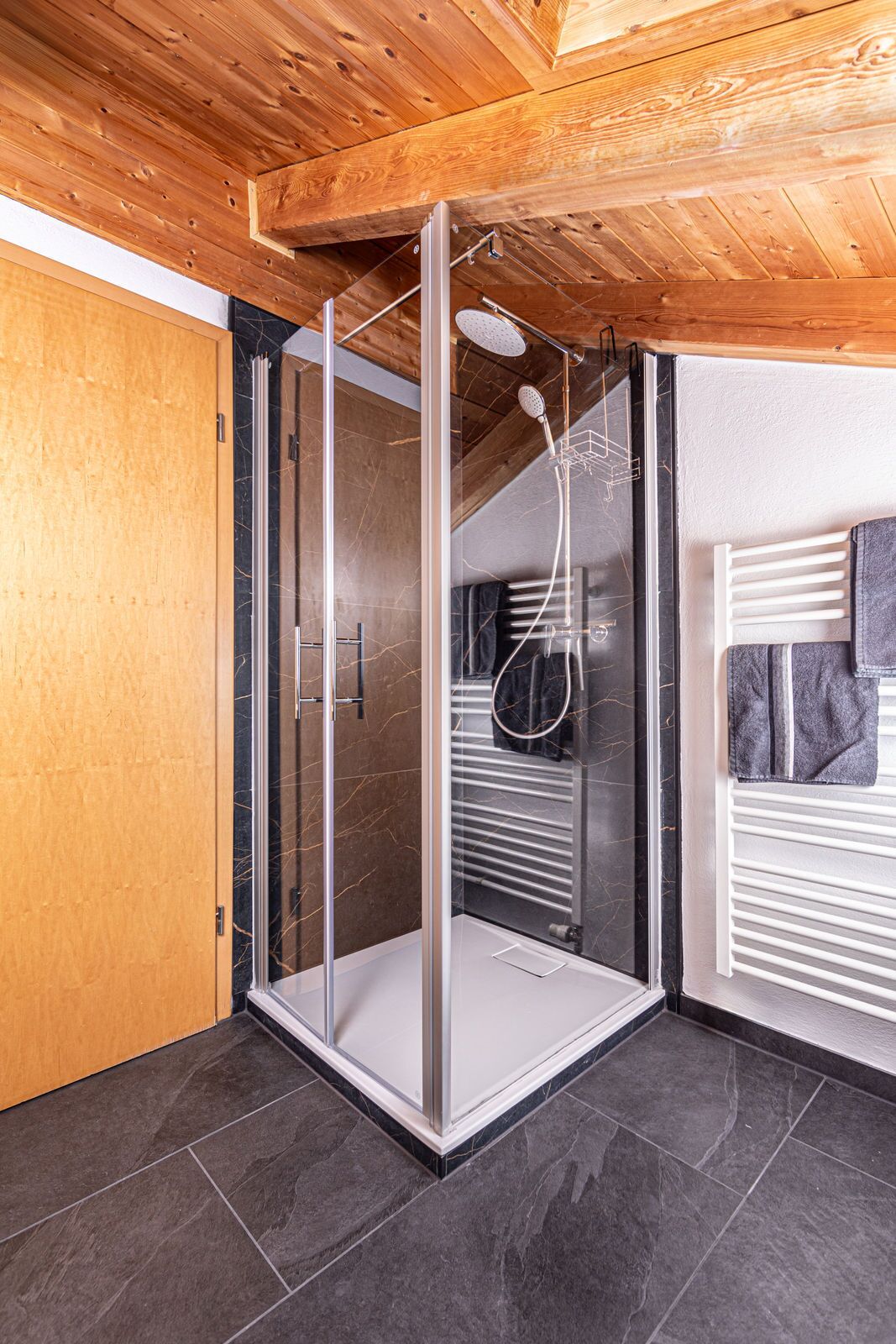 Ein Duschbereich mit Glasabtrennung, Holzboden, Handtuchhalter und Fliesenboden.
