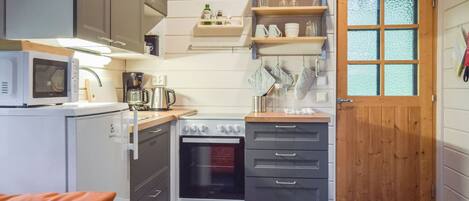 Cozinha compacta com micro-ondas, cafeteira, forno e porta de madeira com painéis de vidro fosco.