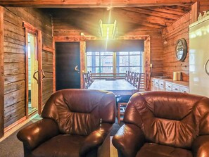 A wooden cabin interior with a dining table and two leather chairs, a large window, and a clock on the wall. - Metsätupa by Interhome (Raasepori)