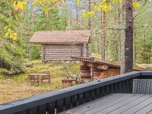 A rustic log cabin with a sloped roof, surrounded by a forest.