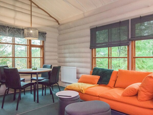 A cozy cabin interior with a dining area, a sofa, and large windows.