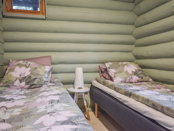 Una habitación tipo cabaña de madera con dos camas, cada una con ropa de cama floral, una pequeña mesa blanca y una ventana sobre la cama izquierda.